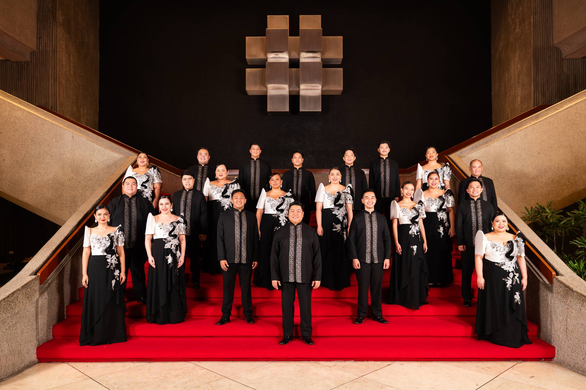 The Philippine Madrigal Singers in formal Filipino attire on a red-carpeted grand staircase